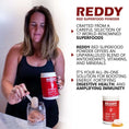 Load image into Gallery viewer, Person pouring Reddy Red Organic Superfood Powder into a smoothie blender, demonstrating its easy mixability and vibrant color.